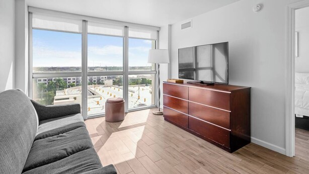 Une chambre d’hôtel moderne dotée d’une grande fenêtre, d’un canapé, d’une armoire en bois et d’un téléviseur à écran plat.