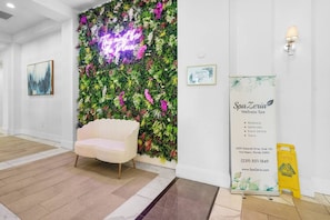 A reception area with a white sofa, a neon sign, a wall-mounted floral decoration, a framed SpaZeria Wellness Spa sign, and a caution sign. - Cozy Apartment in the Heart of Fort Myers (Fort Myers)