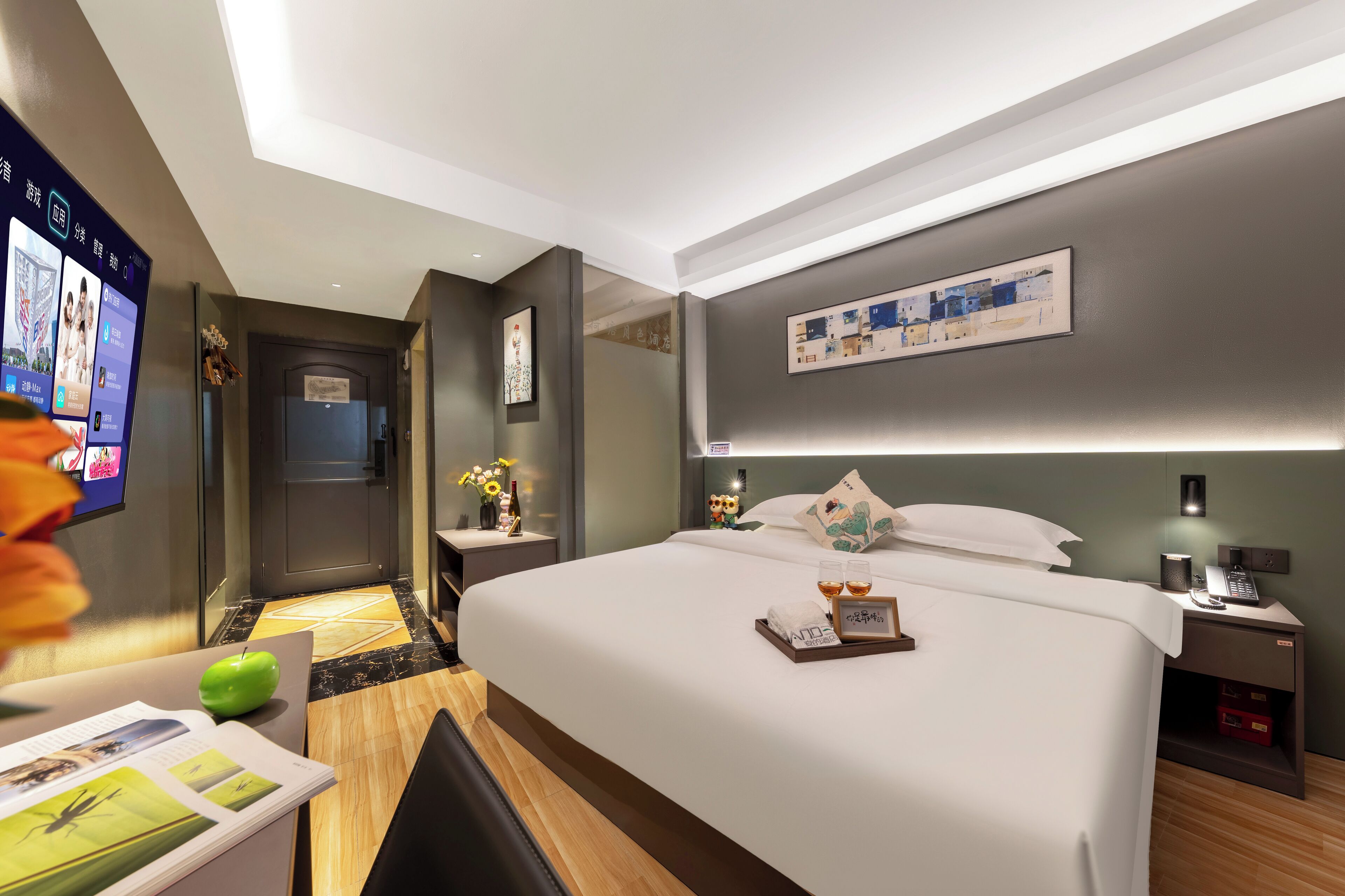 A hotel room with a large bed, bedside tables, a desk with a chair, a TV, and a wall-mounted artwork.