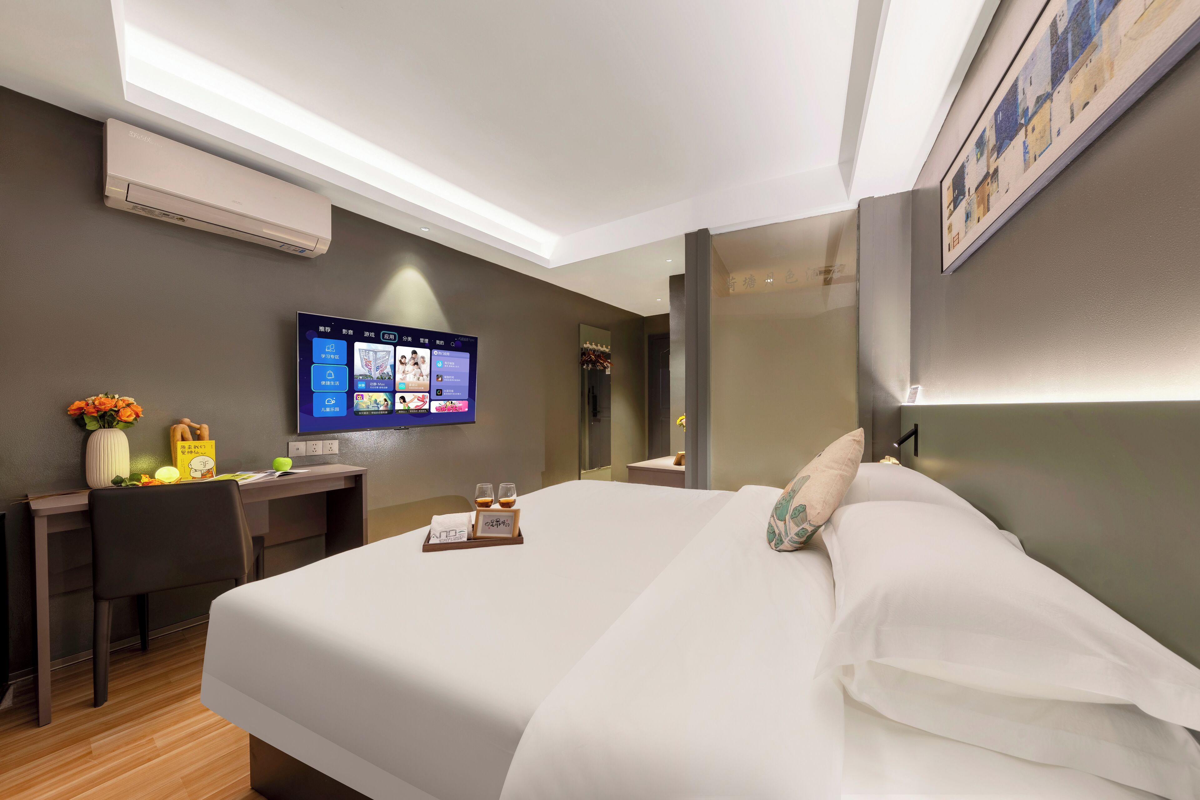 A hotel room with a large bed, a desk with a computer, a flat-screen TV, and a wall-mounted air conditioner.
