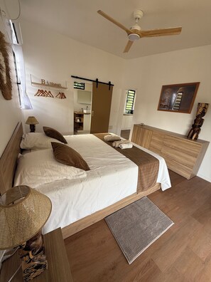 A bedroom with a bed, bedside tables, a ceiling fan, a wardrobe, a mirror, and a framed picture on the wall.