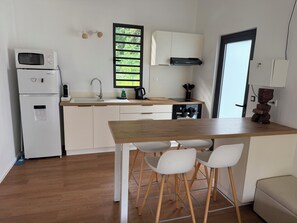 A compact kitchen with a microwave, refrigerator, sink, and wooden dining table with chairs.