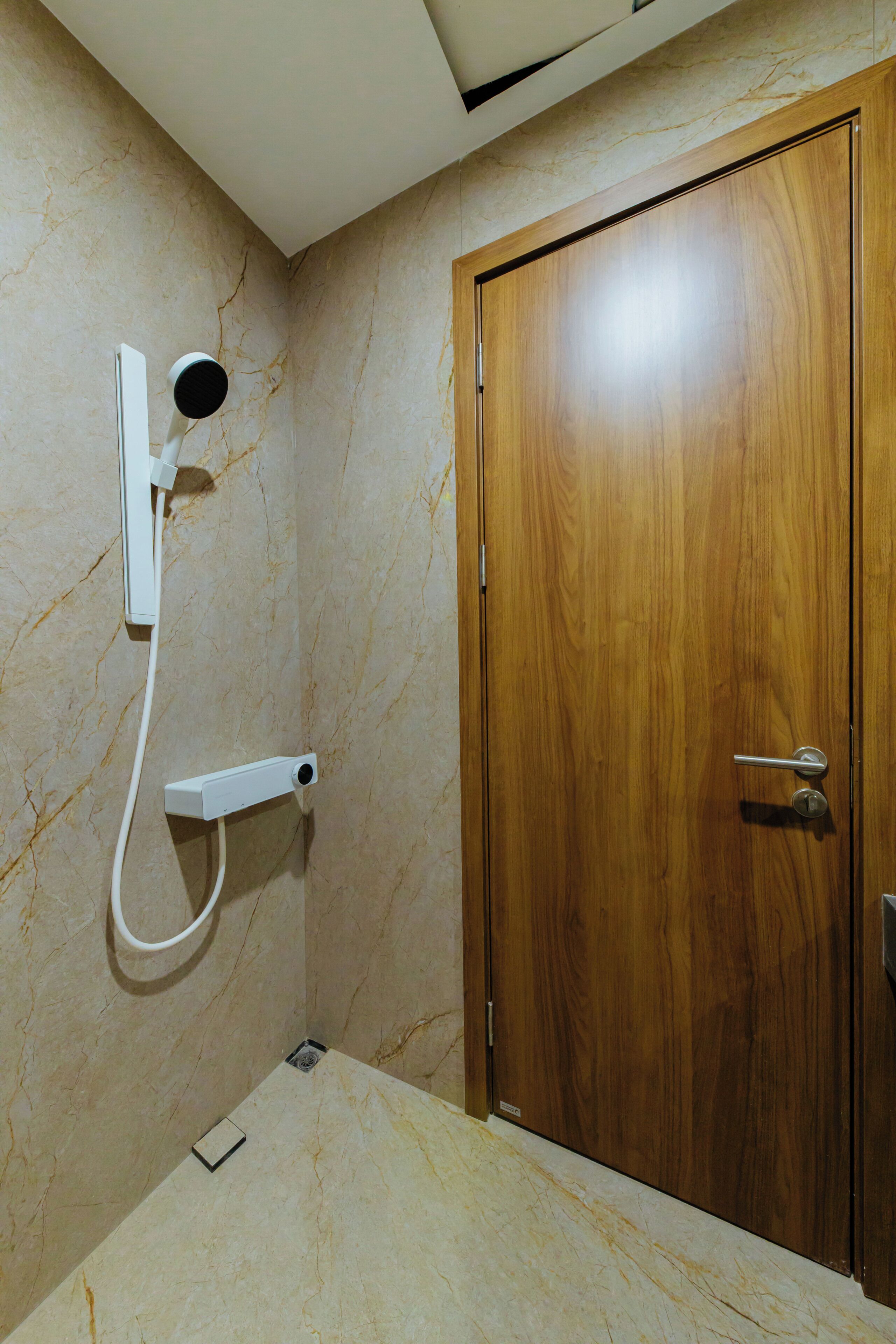 A bathroom with a wooden door, a marble wall, and a shower unit.