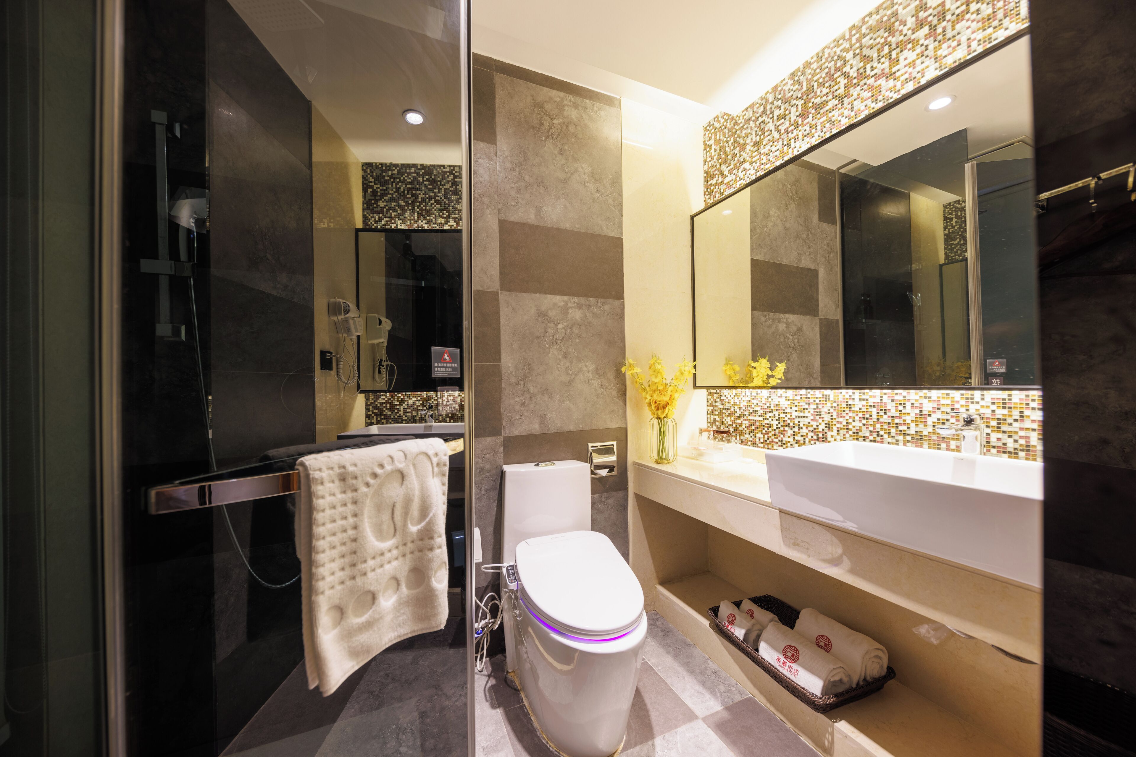 A modern bathroom with a glass-enclosed shower, a white toilet, and a large mirror above a beige vanity.