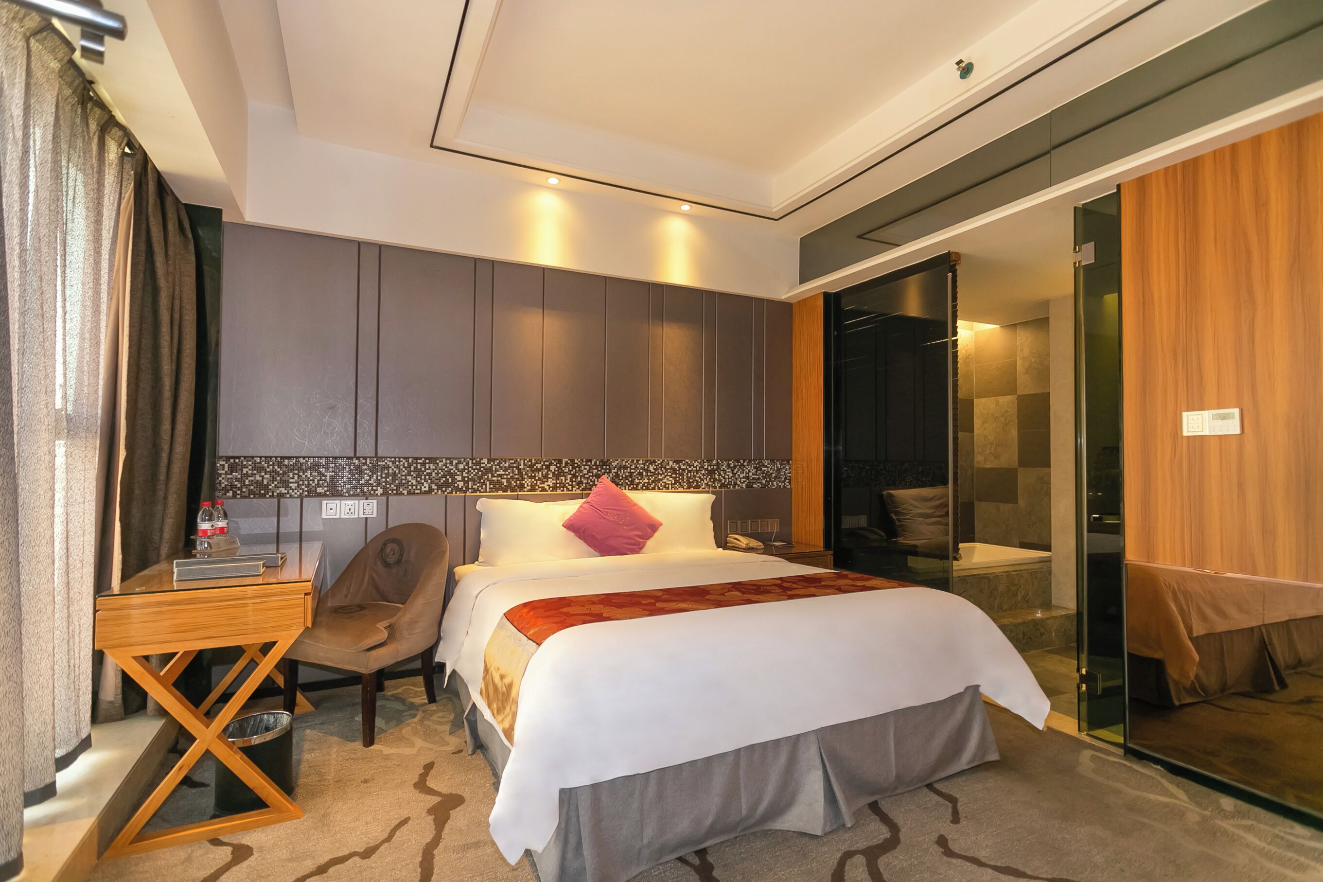 A modern hotel room with a bed, a desk, a chair, a bathroom with a glass door, and a shower area.