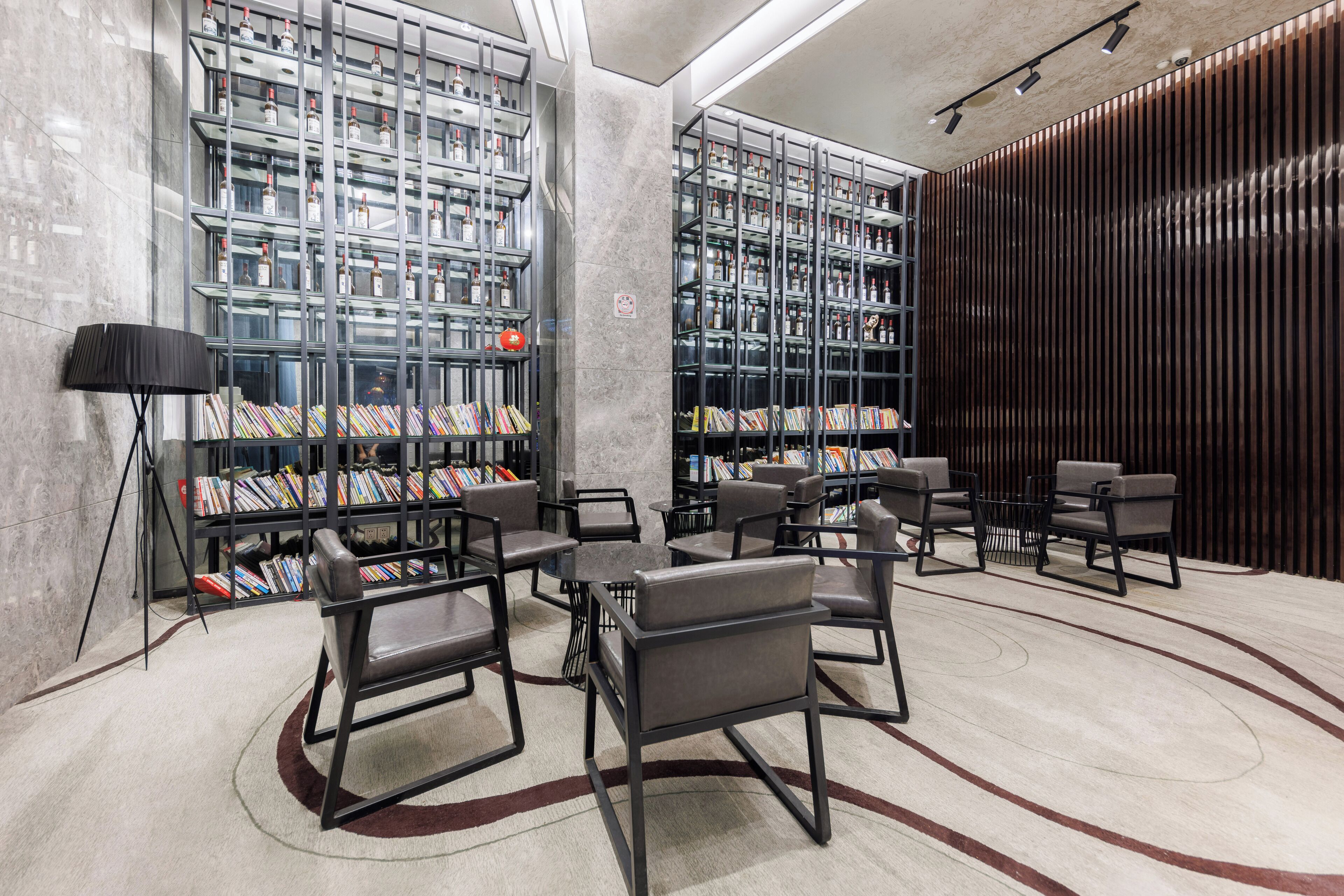 A modern library with bookshelves, comfortable seating, and a patterned carpet.
