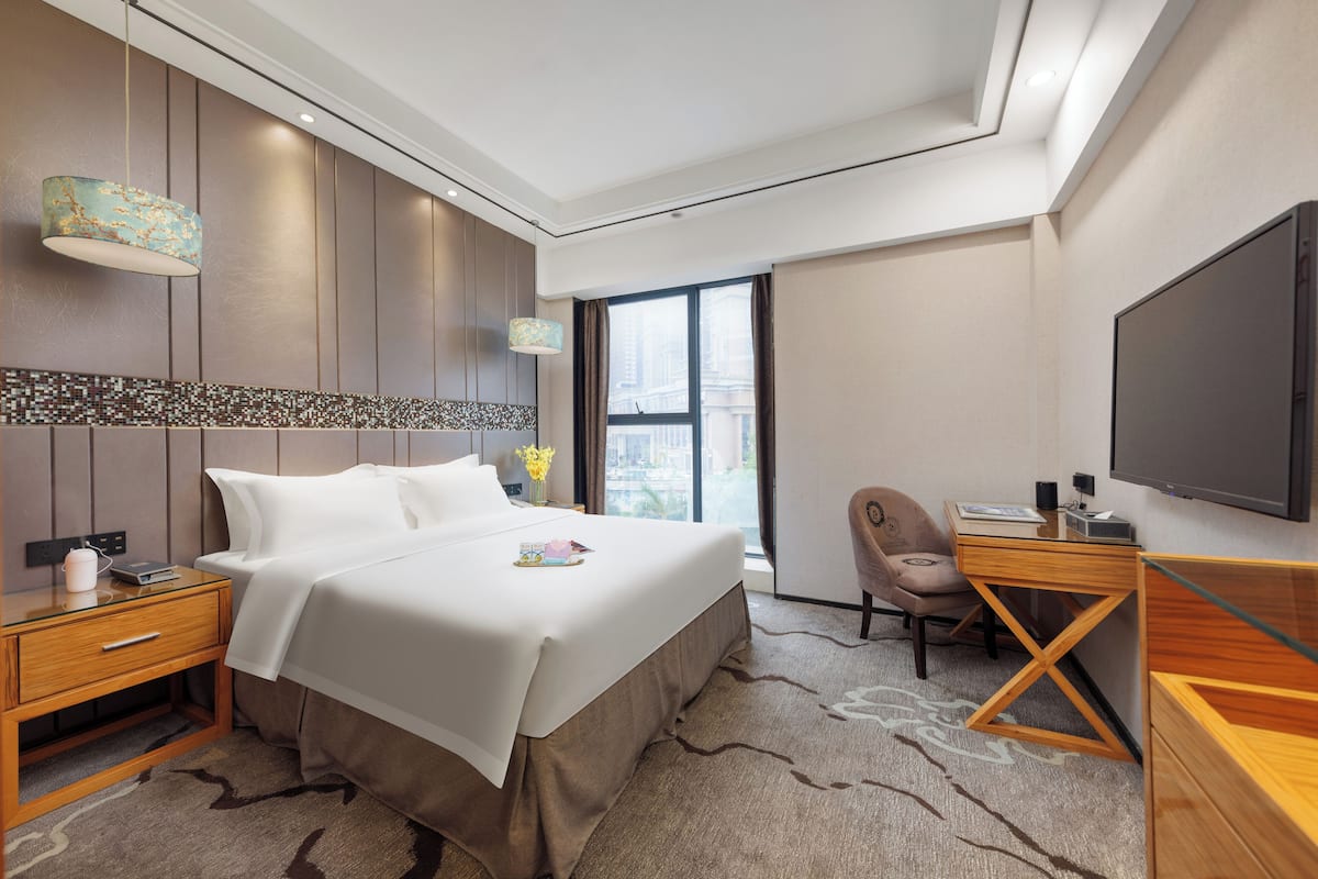 Habitación de hotel con una cama grande, un escritorio, una silla, un televisor y una ventana con vistas a la ciudad.