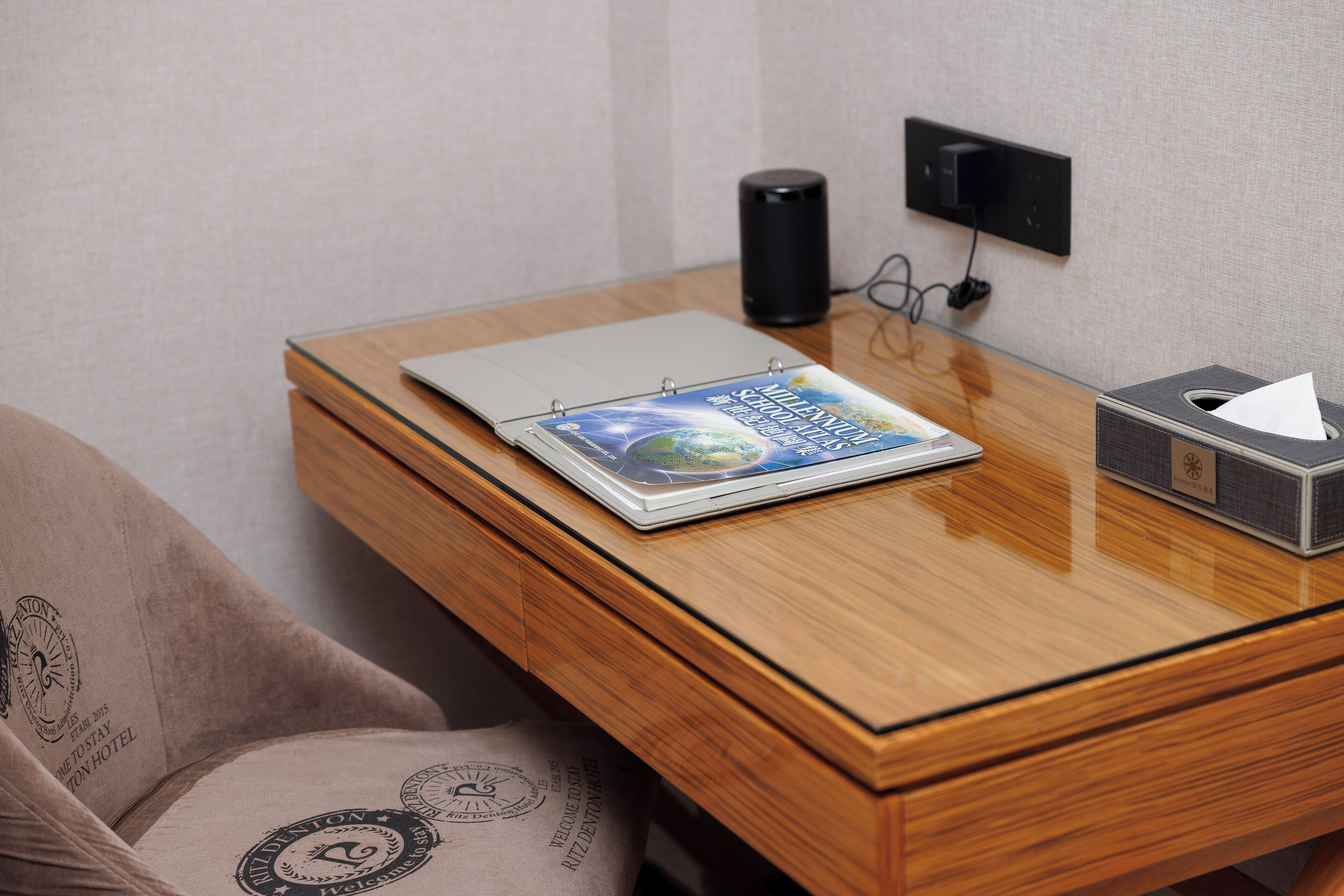 A wooden desk with a laptop, a book, a speaker, and a tissue box.