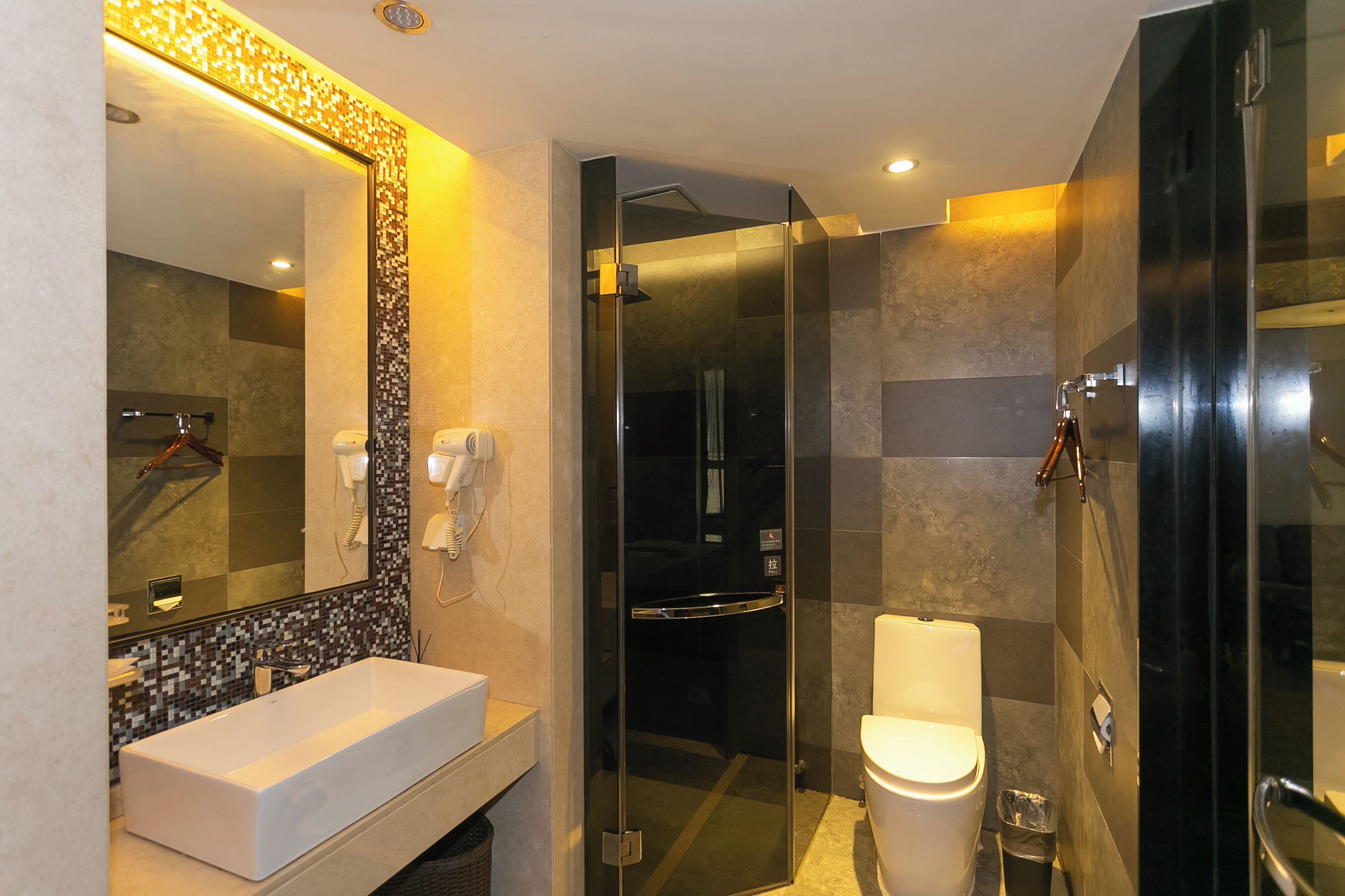 A modern bathroom with a large mirror, a white sink, a glass-enclosed shower, and a toilet.