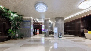 Eine moderne Lobby mit einem großen Chandelier, einem Empfangstresen und einer digitalen Infobüchse.