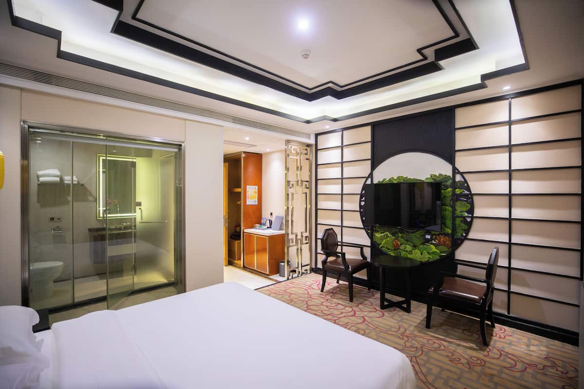 Ein Hotelzimmer mit Bett, Schreibtisch, Stuhl, Fernseher und einer Duschkabine.