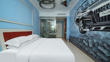 Habitación de hotel con cama, cabecera roja, mural en la pared de un coche Audi y mampara de ducha de cristal.