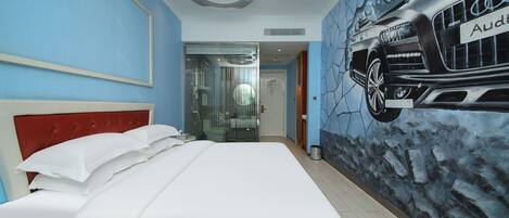A hotel room with a bed, a red headboard, a wall mural of an Audi car, and a glass shower enclosure.