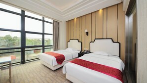 Ein Hotelzimmer mit zwei Betten, großen Fenstern und Blick auf Grünflächen.
