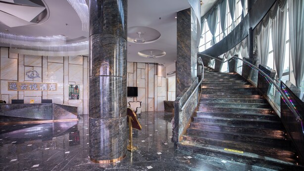 Eine moderne Hotelhalle mit Marmorboden, einem Empfangstresen und einer Treppe zu den oberen Etagen.