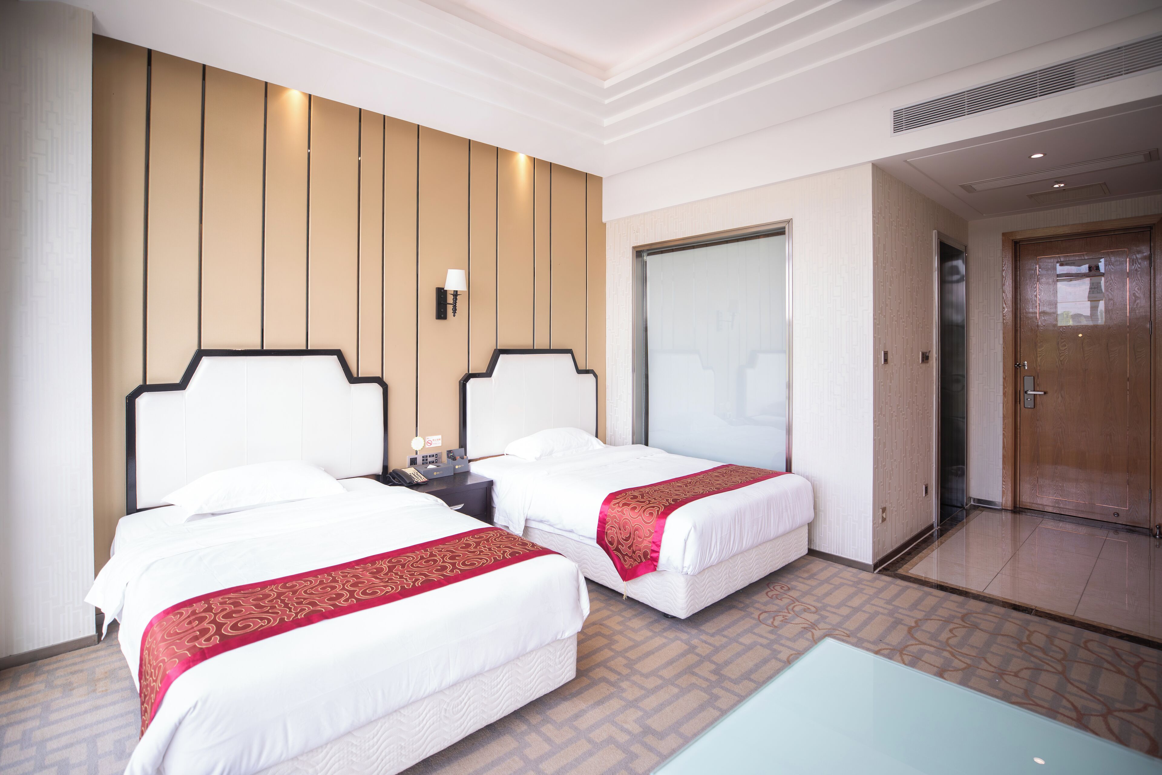 A hotel room with two beds, a nightstand, a lamp, and a large mirror.