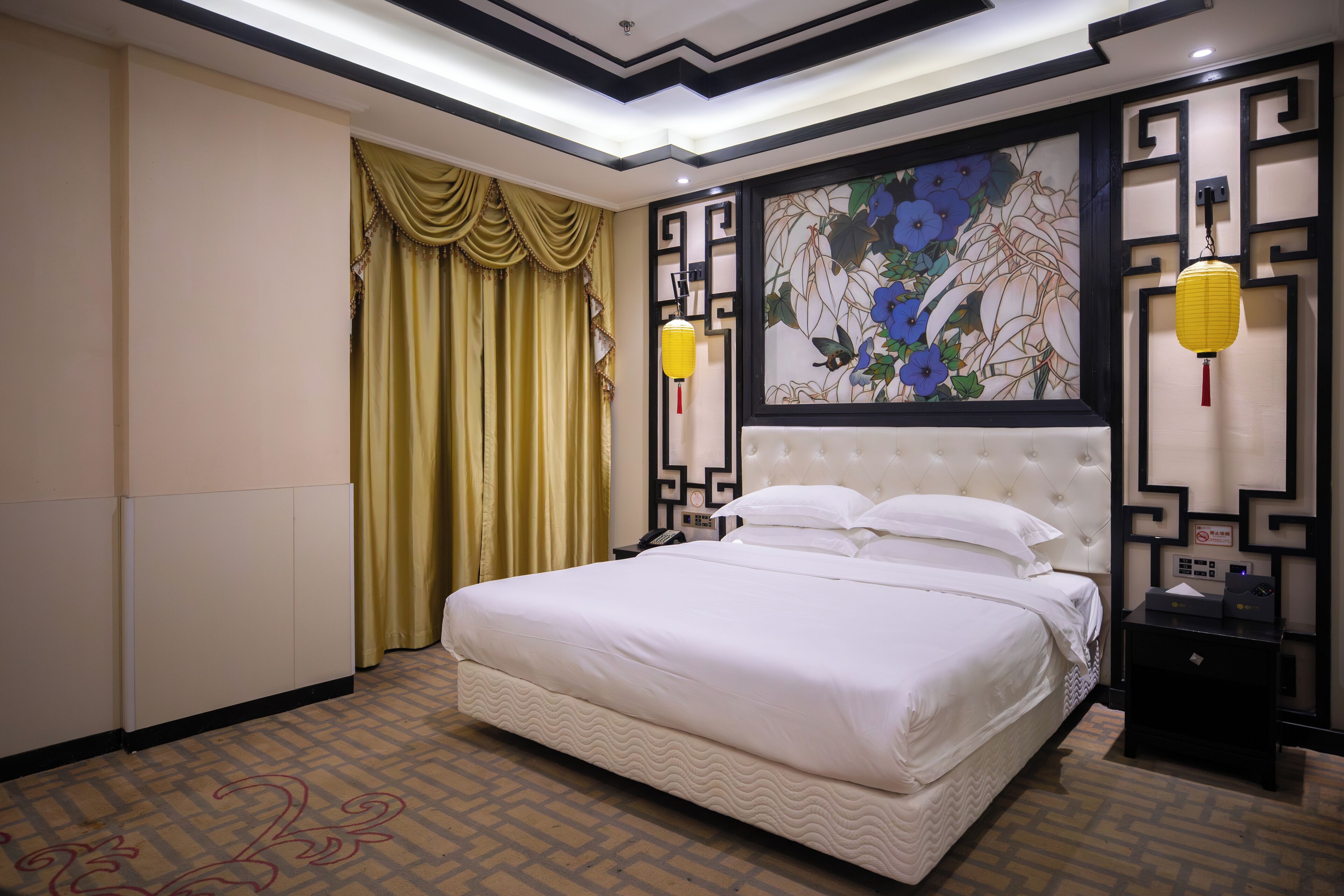 A hotel room with a large bed, a decorative wall with a floral painting, a traditional Chinese-style wall panel, and a nightstand with a lamp.