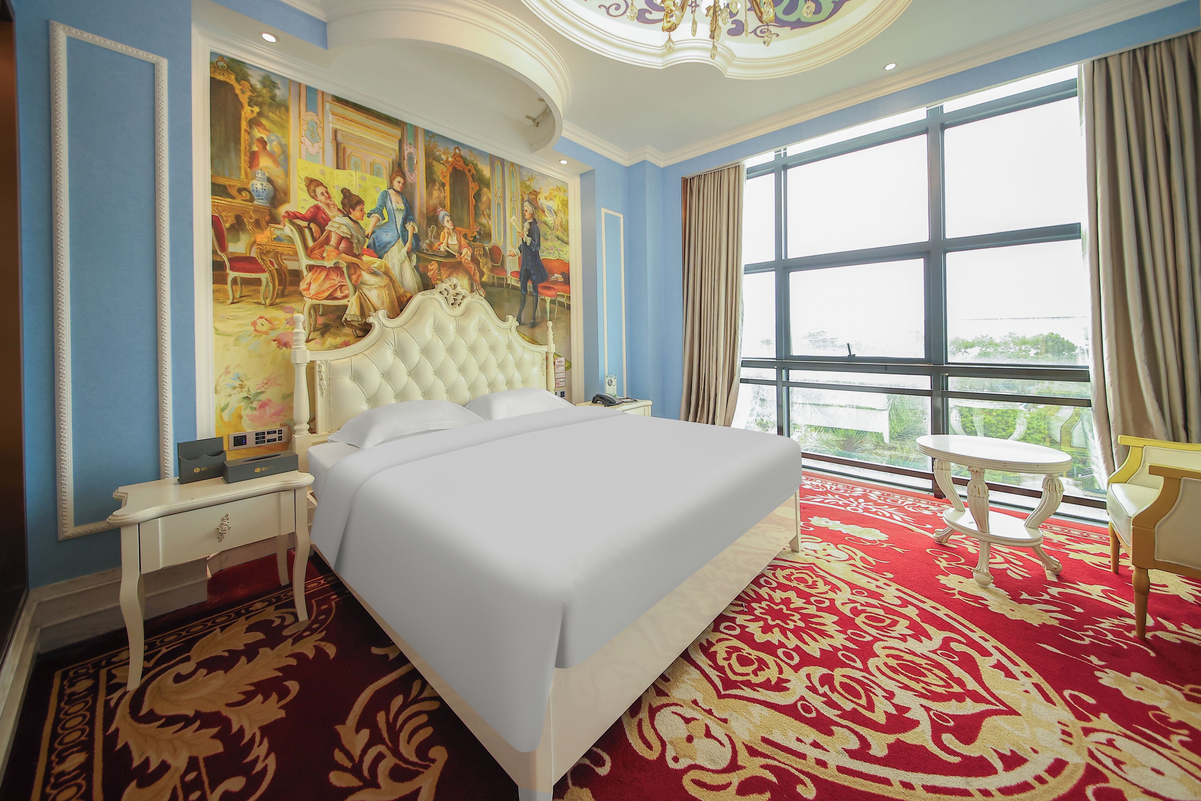 A large bed with a white headboard, a red patterned carpet, and a large window with curtains.