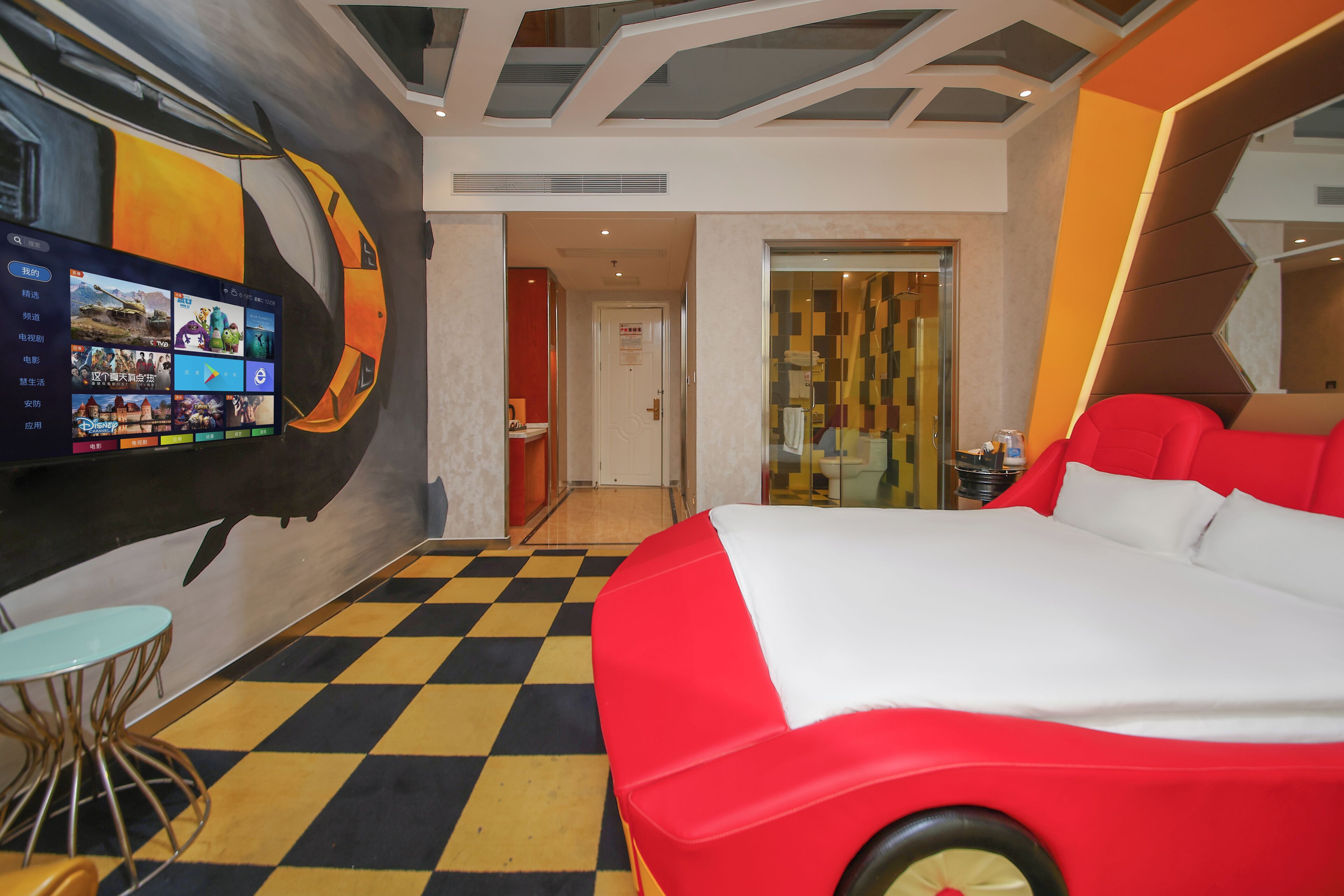 Une chambre d’hôtel avec un sol à carreaux, un grand lit aux motifs rouges et blancs, un téléviseur fixé au mur et un design moderne au niveau du plafond.