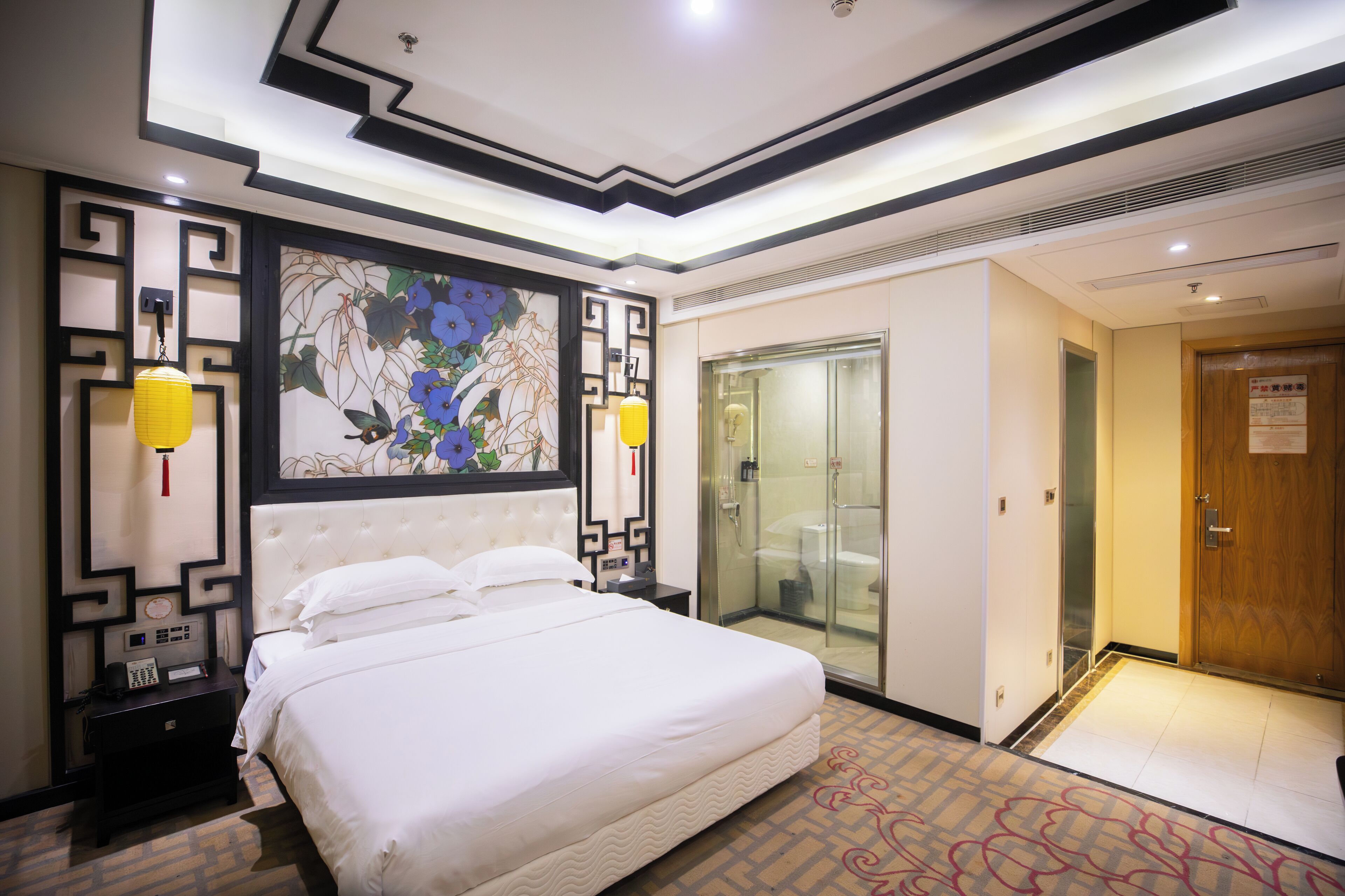 A hotel room with a large bed, a decorative wall, a glass shower enclosure, and a wooden door.