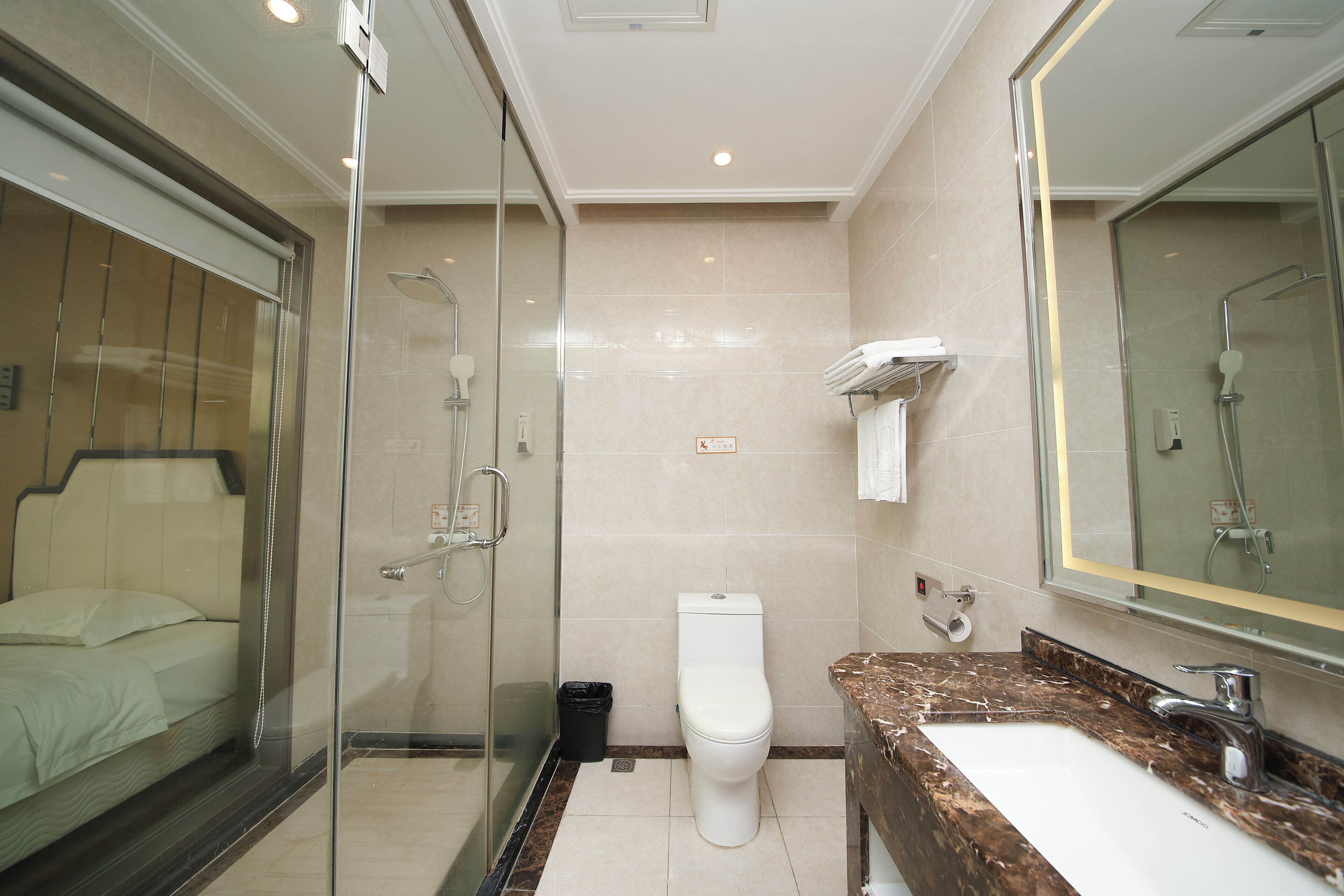 A hotel bathroom with a glass-enclosed shower, a toilet, and a sink with a marble countertop.