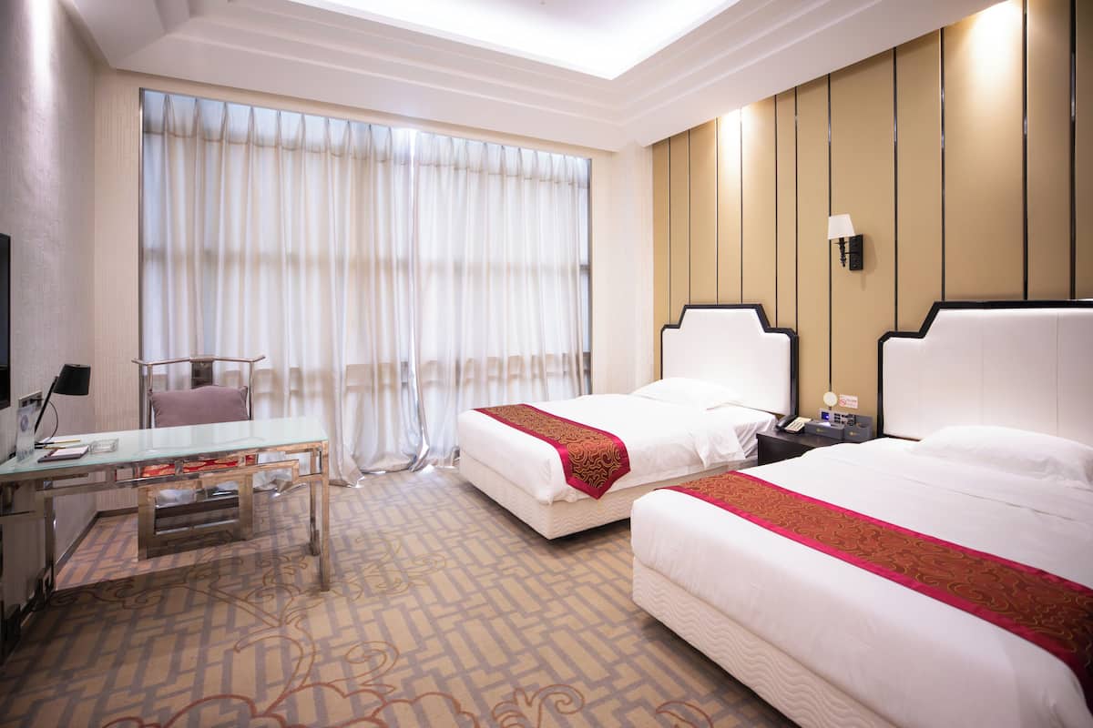 Ein Hotelzimmer mit zwei Betten, einem Schreibtisch, einem Sessel und einem großen Fenster mit Vorhängen.