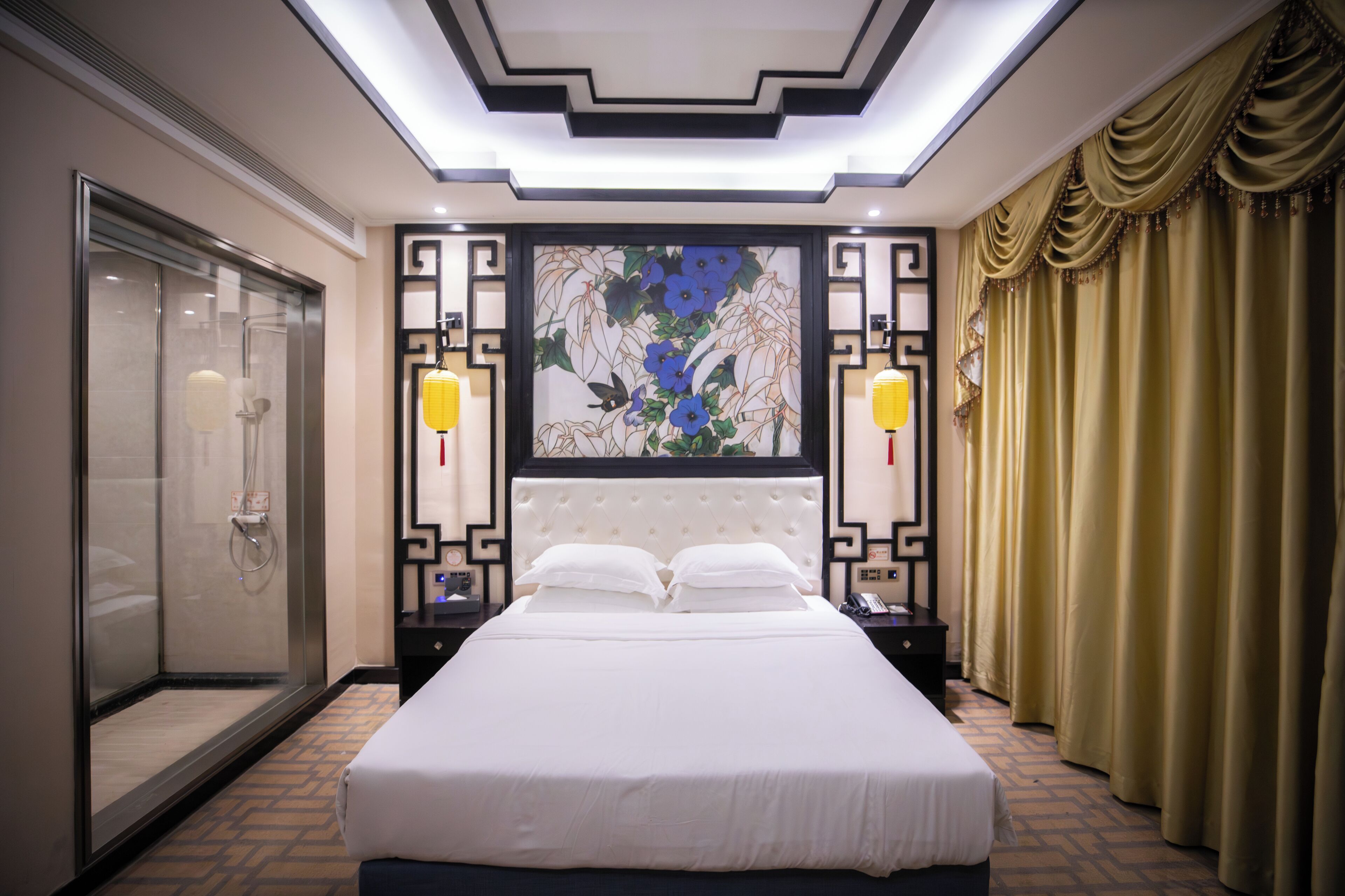 A hotel room with a large bed, a glass-enclosed shower, and a decorative wall with a floral pattern.