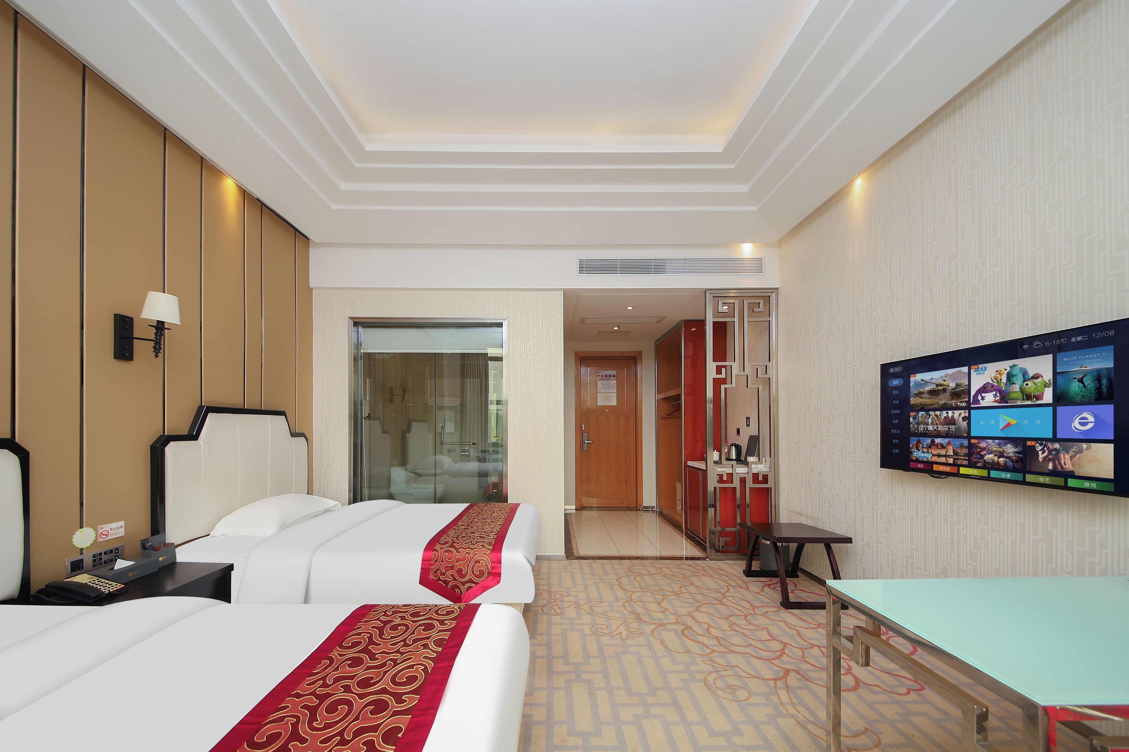 Habitación de hotel con dos camas, televisión, escritorio y baño visible a través de un vidrio.