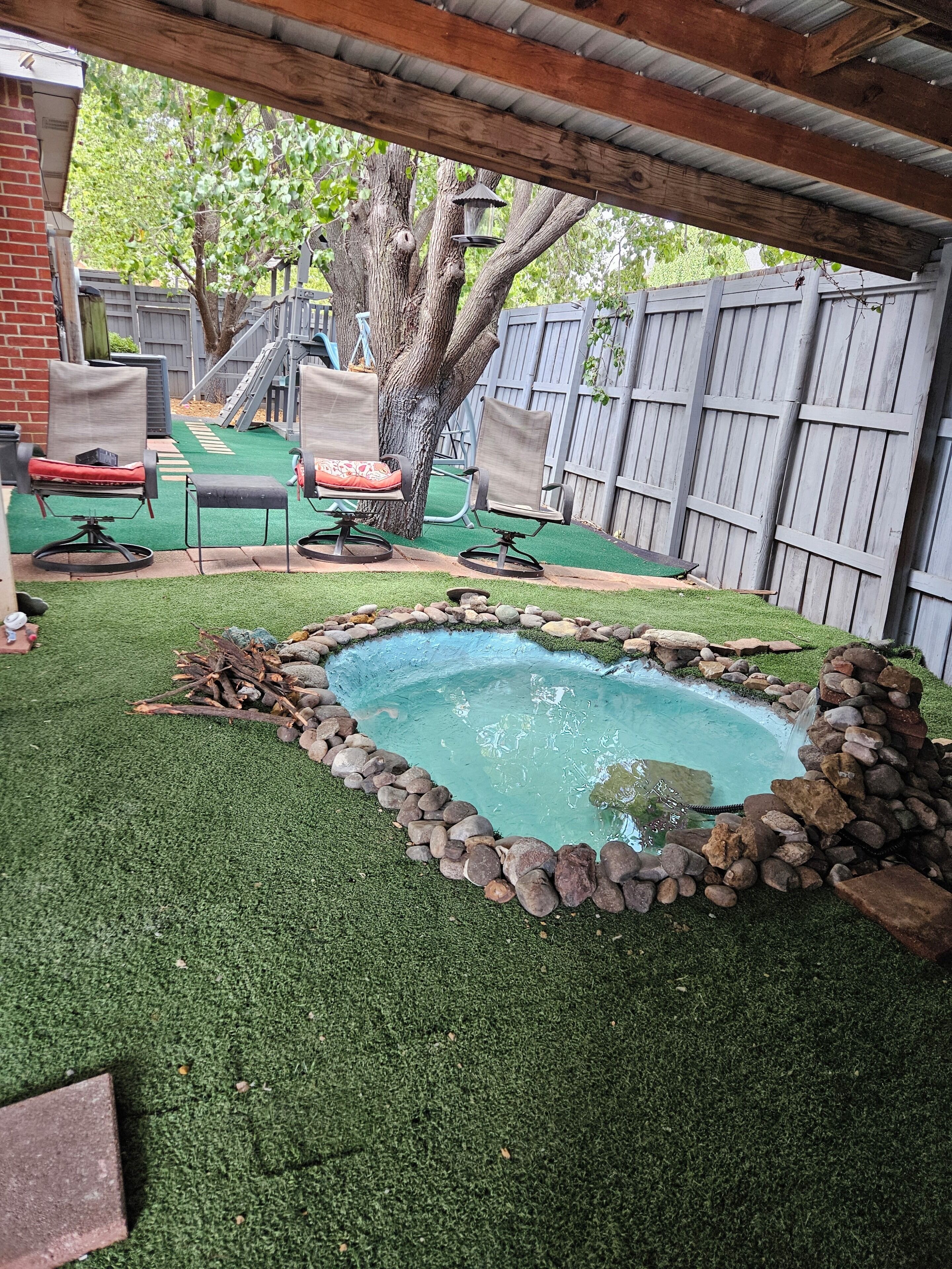 Un jardin avec une petite piscine entourée de rochers, de gazon synthétique et d’une terrasse en bois.