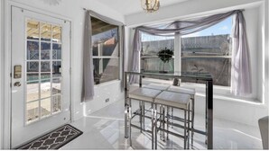 Una habitación luminosa con puerta de cristal, ventanas amplias, una araña y una mesa con sillas.