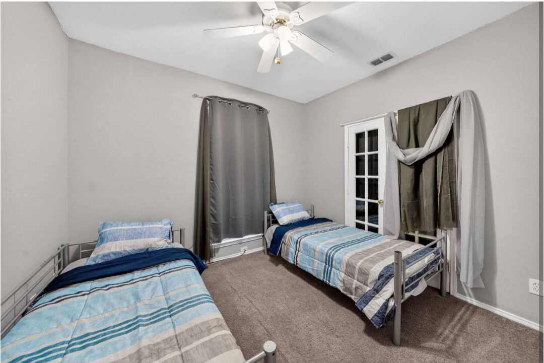 Un dormitorio con dos camas individuales, ventilador de techo, ventana con cortinas y una puerta.