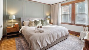 Une chambre à coucher bien aménagée, avec un grand lit, deux tables de chevet avec des lampes, une fenêtre avec des stores et un plancher en bois.