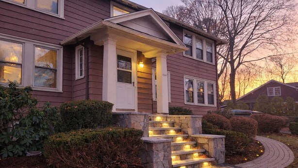 A two-story house with a stone staircase leading to the front door, surrounded by well-maintained bushes and a brick pathway. - Prestigious Milton Designer Home (Milton)