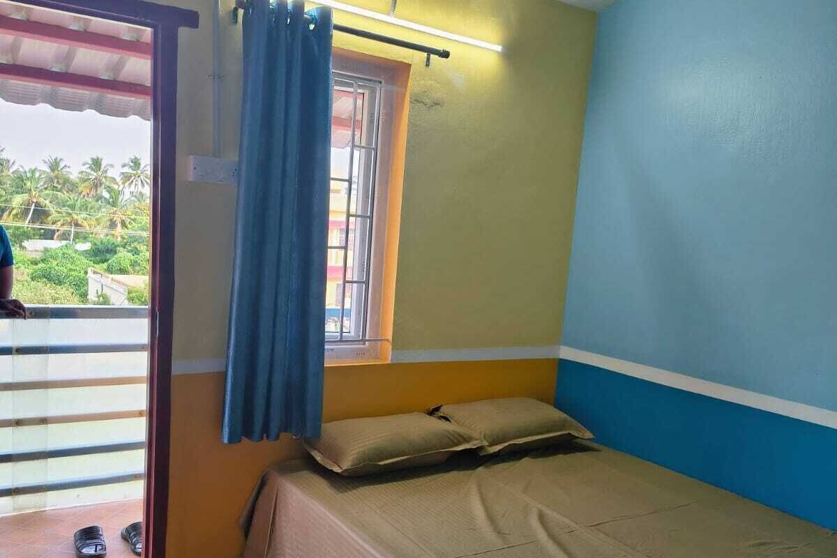 Un dormitorio con una cama, una ventana con cortina, una puerta que da a un balcón y suelo de madera.