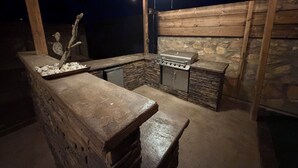 Cozinha externa com bancada de pedra, churrasqueira e ventilador de teto.