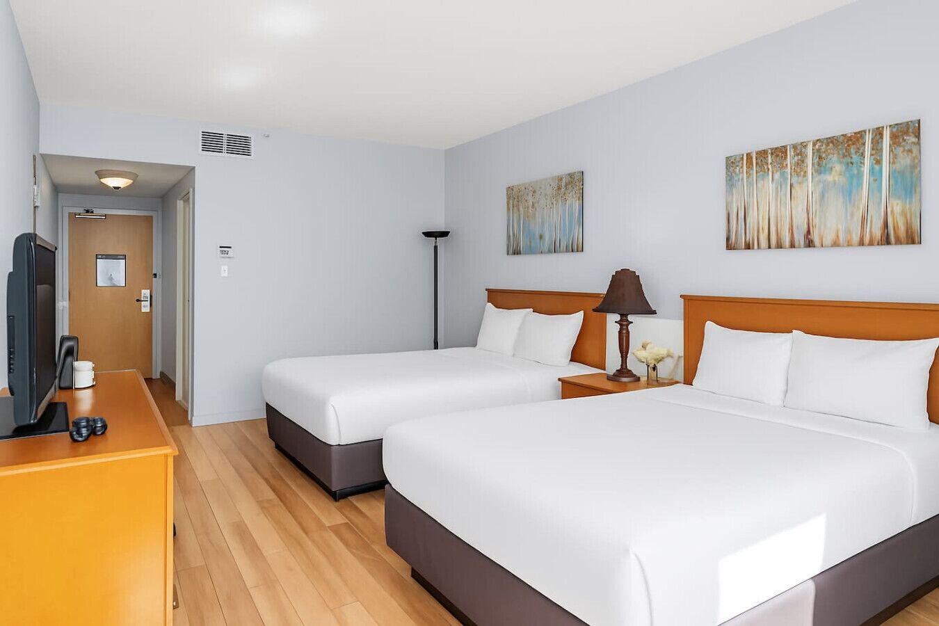 A hotel room with two beds, a desk with a TV, and artwork on the walls.
