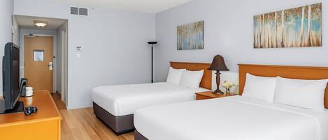 A hotel room with two beds, a desk with a TV, and artwork on the walls.