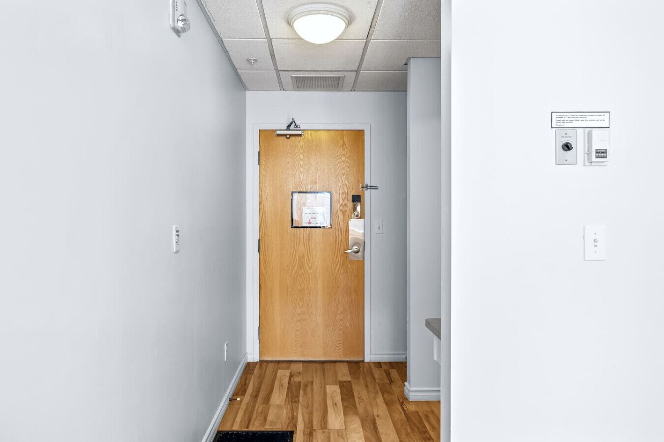 Un pasillo con una puerta de madera, un interruptor de luz y un termostato en la pared.