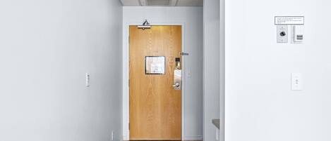 Un pasillo con una puerta de madera, un interruptor de luz y un termostato en la pared.