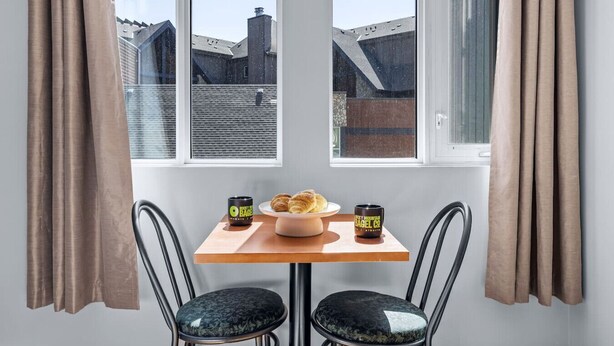 Un coin repas comprenant une table, deux chaises et une vue sur les bâtiments, visible à travers de grandes fenêtres.