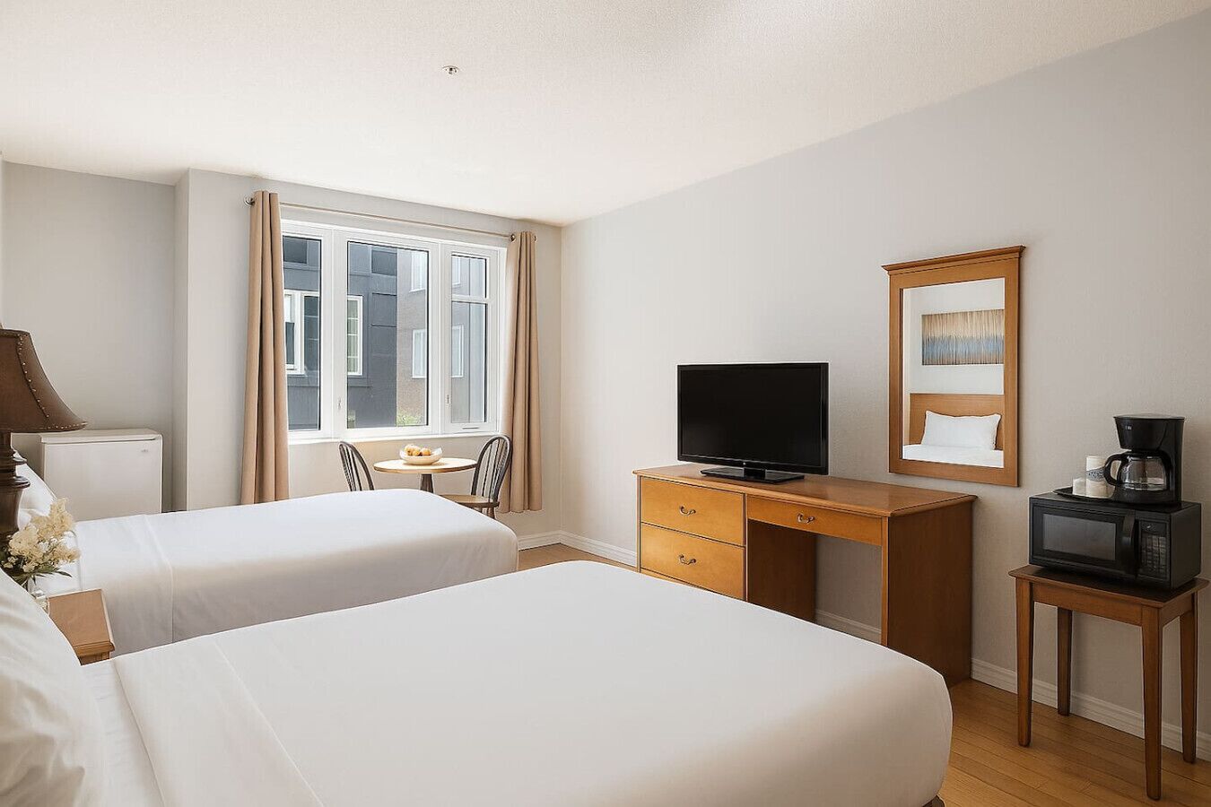 A hotel room with two beds, a desk with a TV, a coffee maker, and a window with curtains.