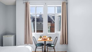 Une chambre avec un lit, une petite table sur laquelle sont disposés des éléments pour le petit-déjeuner, deux chaises et une fenêtre avec des rideaux.