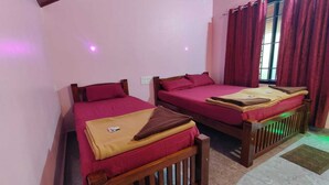 Una habitación con dos camas de madera, cada una con una colcha roja y una manta marrón. Tiene una ventana con cortinas rojas, y el suelo es de baldosas.