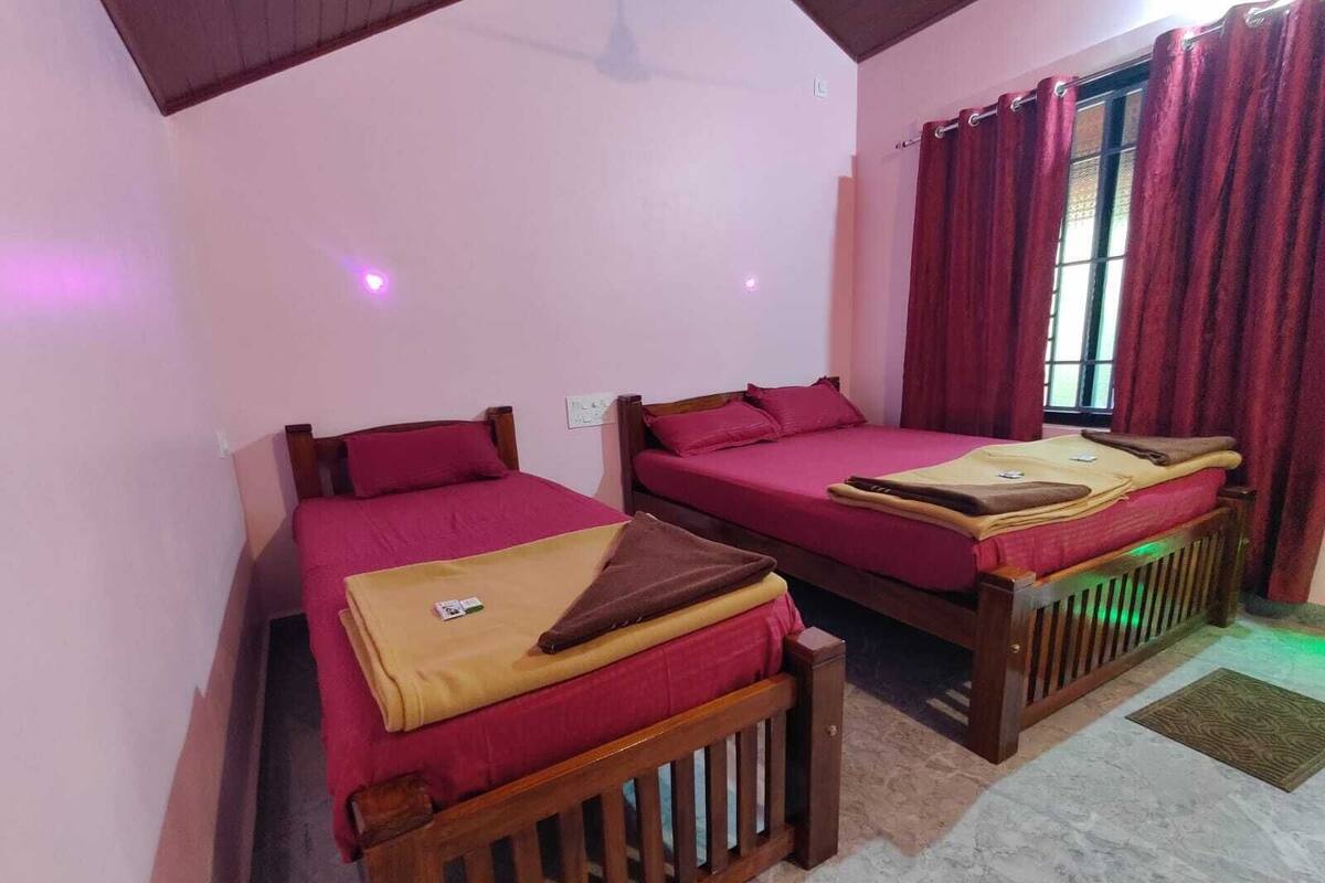 A room with two wooden beds, each with a red bedspread and a brown blanket. There is a window with red curtains, and the room has a tiled floor.