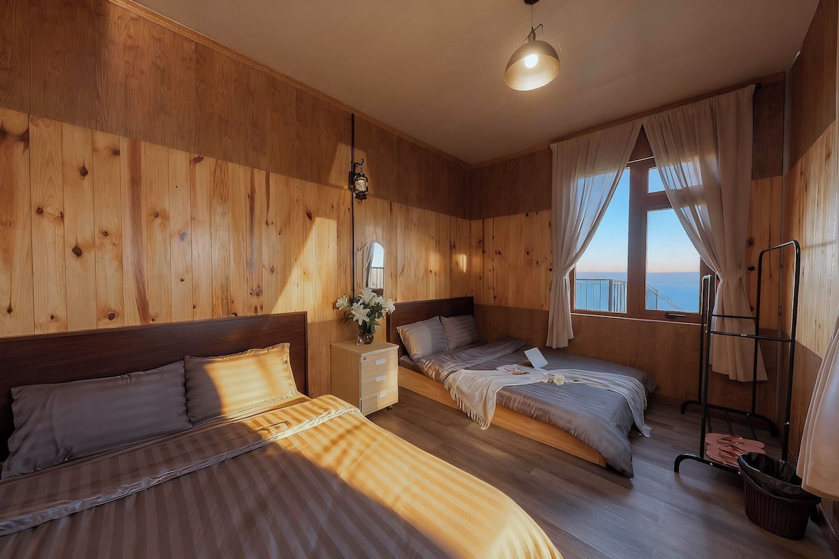 Una habitación con paneles de madera, dos camas, una mesita de noche, una lámpara y un ventanal con vistas.