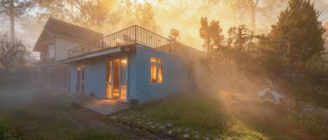 Una casa moderna con balcón, rodeada de árboles y niebla.
