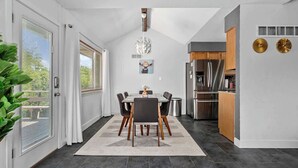 Una cocina moderna con baldosas oscuras, una zona de comedor con mesa y sillas, y vistas a través de la puerta de cristal.