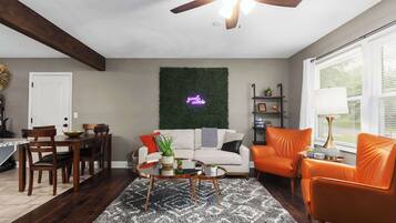 A living room with a white sofa, an orange armchair, a coffee table, and a ceiling fan.