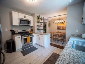 A modern kitchen with white cabinetry, a stainless steel stove, and a granite countertop. There is a small trash can and a rug on the floor. - Sleeps 7_3BR W/Queen Beds_Near KC Attractions (Kansas City)