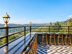 A terrace with a glass balustrade, a row of bar stools, and two street lamps. - Hotel Celestial Ganges (Rishikesh)
